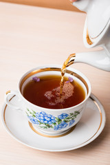 Old-style porcelain kettle pouring tea from jug to cup of tea