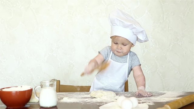 The little boy in a suit of the cook sculpts dough. Baby make dinner in chef suit