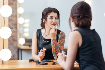 Fototapeta premium Beautiful tattooed woman applying lipstick in dressing room
