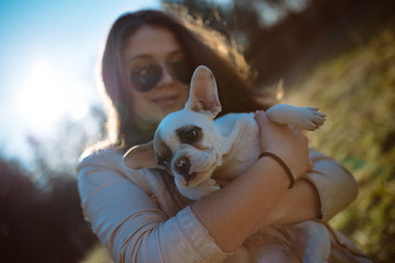 Young girl playing with a French bulldog puppy in a park.
