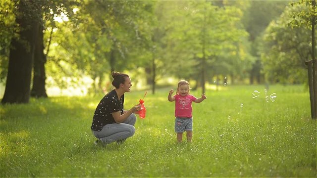 Mother and girl blowing soap bubbles outdoor. Parent and kid having fun in park.