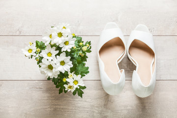 Closeup of a pair of white high heel womens shoes and Beautiful flowers white chrysanthemum on wooden background.
