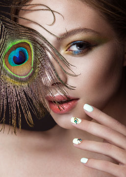 Beautiful girl with bright makeup, manicure design and peacock feather on her face. Art nails.