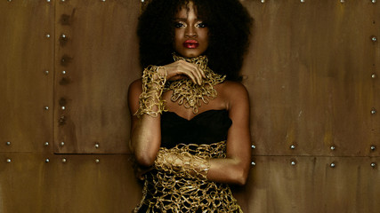 Luxurious portrait of sexy african american female model with glossy golden makeup posing to the...