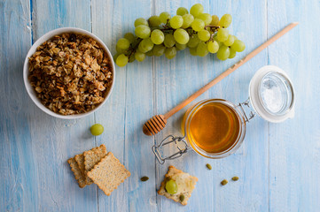 Breakfast cereals with grapes, honey and muesli on a blue background, top view