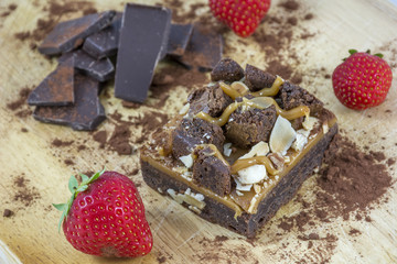 One piece of brownie with chocolate and several strawberries on the light wooden background