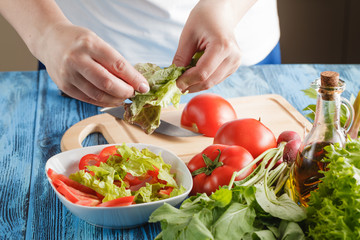 Cook is tearing lettuce while making fresh summer salad, closeup