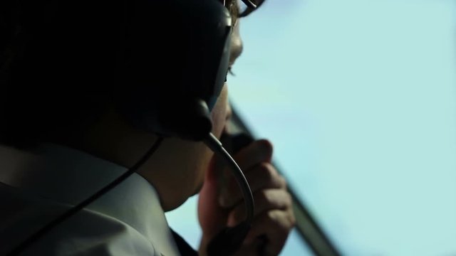 Serious male pilot focused on flight navigation, talking to air controller