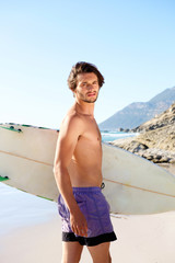 Young guy standing at the beach with surfboard