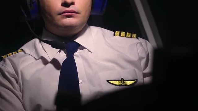 Man in civil aviation pilot uniform and headset navigating aircraft at cockpit