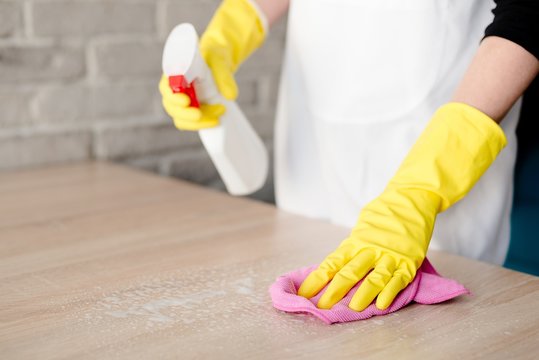 Woman in yellow rubber gloves cleaning table