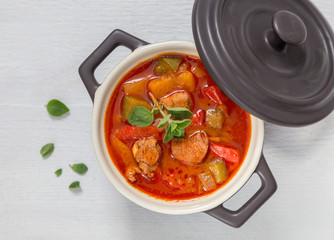 Gulasch in einer schwarzen cocotte mit Majoran auf weißem Holz