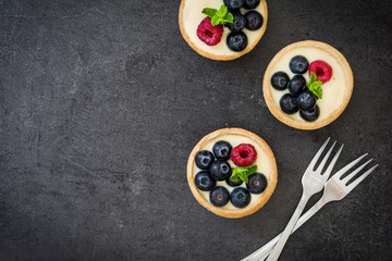 Delicious tartlets with raspberries and blueberries on slate background
