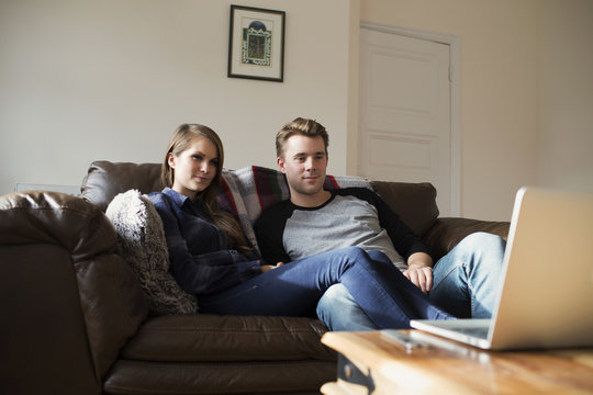 Young Couple Watching Movie Streamed To Laptop At Home