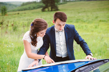 Young couple after the wedding goes on a journey to the blue car. The boy and girl studying a map and route planning