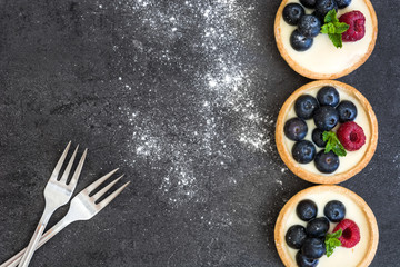 Delicious tartlets with raspberries and blueberries on slate background

