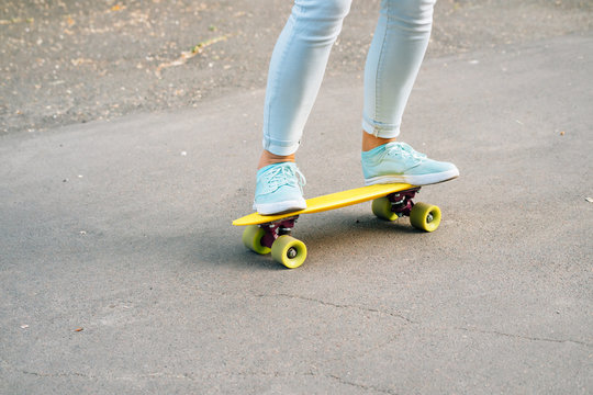 Close-up of female legs in jeans and sneakers riding a skateboar