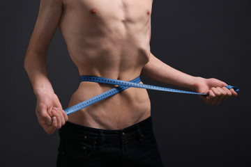 Young man measuring himself on dark background