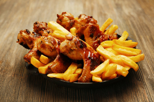 Baked chicken wings with French fries on wooden table