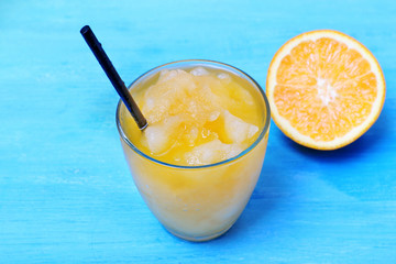 Glass of orange juice with crushed ice on blue wooden table