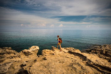 Young woman hiker standing on top of the rocks and enjoying view of a Blue Lagoon near Polis city, Akamas Peninsula National Park, Cyprus