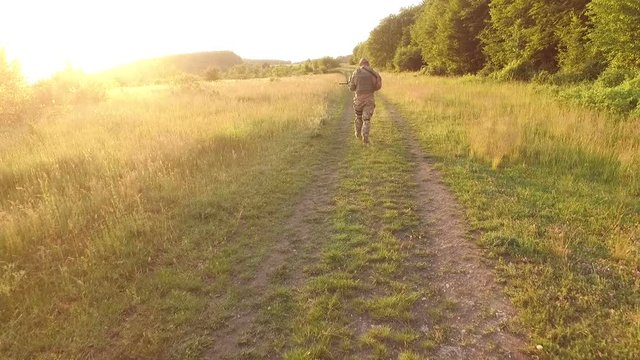 Aerial view: Soldier goes on path in the field. Camera behind him