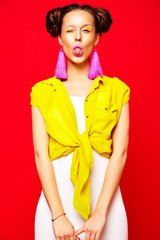 portrait of cheerful fashion hipster girl in casual colorful vivid hipster yellow summer clothes on red background showing her tongue