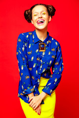 portrait of cheerful fashion hipster girl in casual colorful vivid hipster blue and yellow summer clothes on red background  showing her tongue