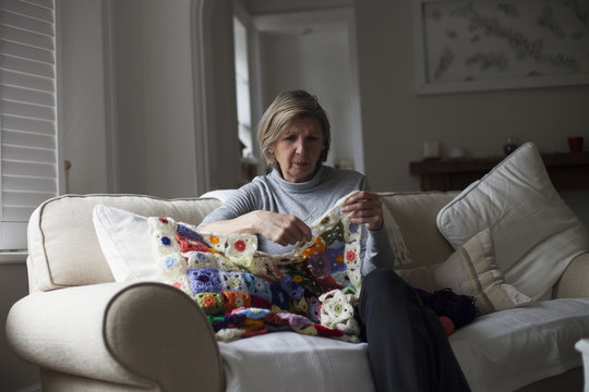 Close Up Of Woman Sitting On Sofa Making Crochet Blanket