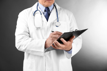 Professional doctor with clipboard on grey background