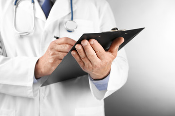 Professional doctor with clipboard on grey background