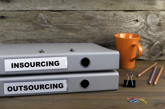 Insourcing and Outsourcing - two folders on wooden office desk