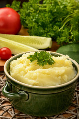 Mashed potatoes in green ceramic pot on wooden background.