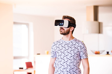 Man wearing virtual reality goggles, standing in living room