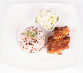 Pork chop (covered in breadcrumbs), three color rice and cucumber salad decorated with dill on a plate on white background