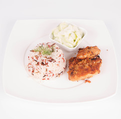 Pork chop (covered in breadcrumbs), three color rice and cucumber salad decorated with dill on a plate on white background