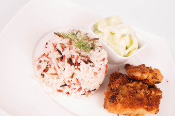 Pork chop (covered in breadcrumbs), three color rice and cucumber salad decorated with dill on a plate on white background