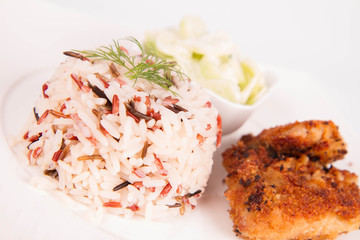 Pork chop (covered in breadcrumbs), three color rice and cucumber salad decorated with dill on a plate on white background