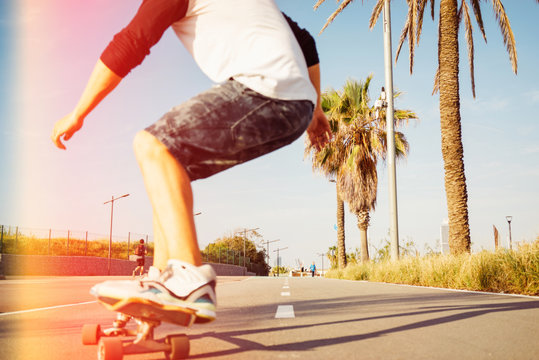 A man is skateboarding in a urban area with his back to the camera. Motion photo of a young guy on a longboard in a skatepark. Street photo with focus on landscape and flare light.