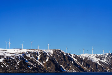 Wind Energy in Norway. The blue sea and gray cliff covered with snow on the background of a cloudless sky