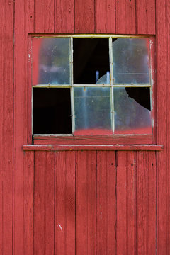 Broken window on barn with red siding