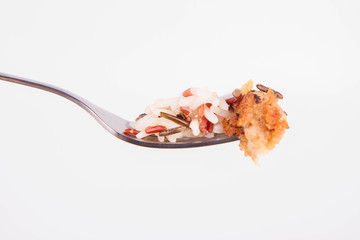 Piece of pork chop (covered in batter and breadcrumbs) and some three color rice on a fork on white background