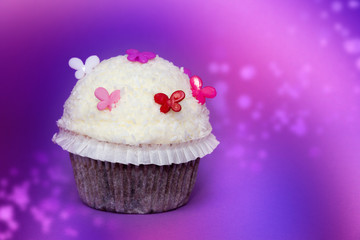 Kokosnuss Cupcake mit violettem Hintergrund und Schmetterlingen dekoriert