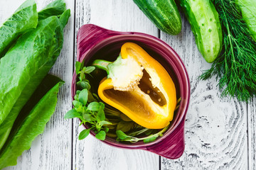 Fresh vegetables - cucumber, pepper, salad, basil, dill in a bowl and rustic background, top view