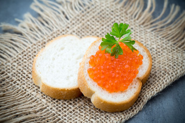 Bread with fresh cream cheese and red caviar on table.