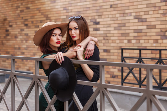 Beautiful fashion women posing. Trendy lifestyle urban portrait on city background. Girls wearing in style clothes, hats and accessories