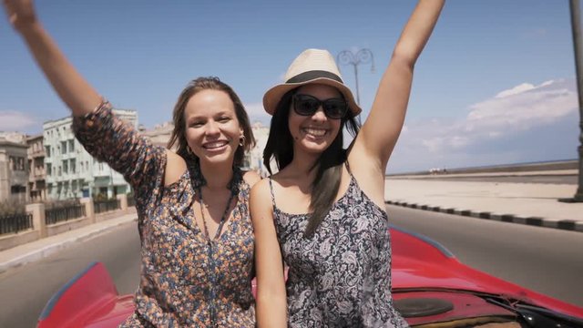 Female friends on holidays, people traveling, young women having fun on vacation, two happy girls smiling in Havana, Cuba, laughing on old classic convertible car, blowing kiss. Slow motion