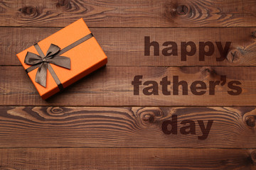 Orange box with brown ribbon on wooden background. Fathers day