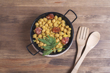 Close-up of nutritious chickpeas with codfish and sausage on plate.Fork and spoon.From above.