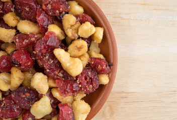 Top close view of cranberries and walnuts in a small bowl on a wood table top